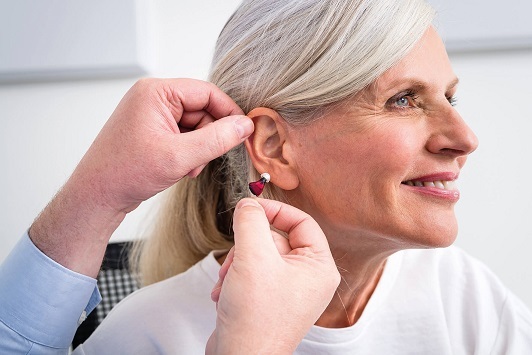 Ältere Frau bekommt von einem Hörakustiker ein modernes Hörgerät angepasst und testet es.